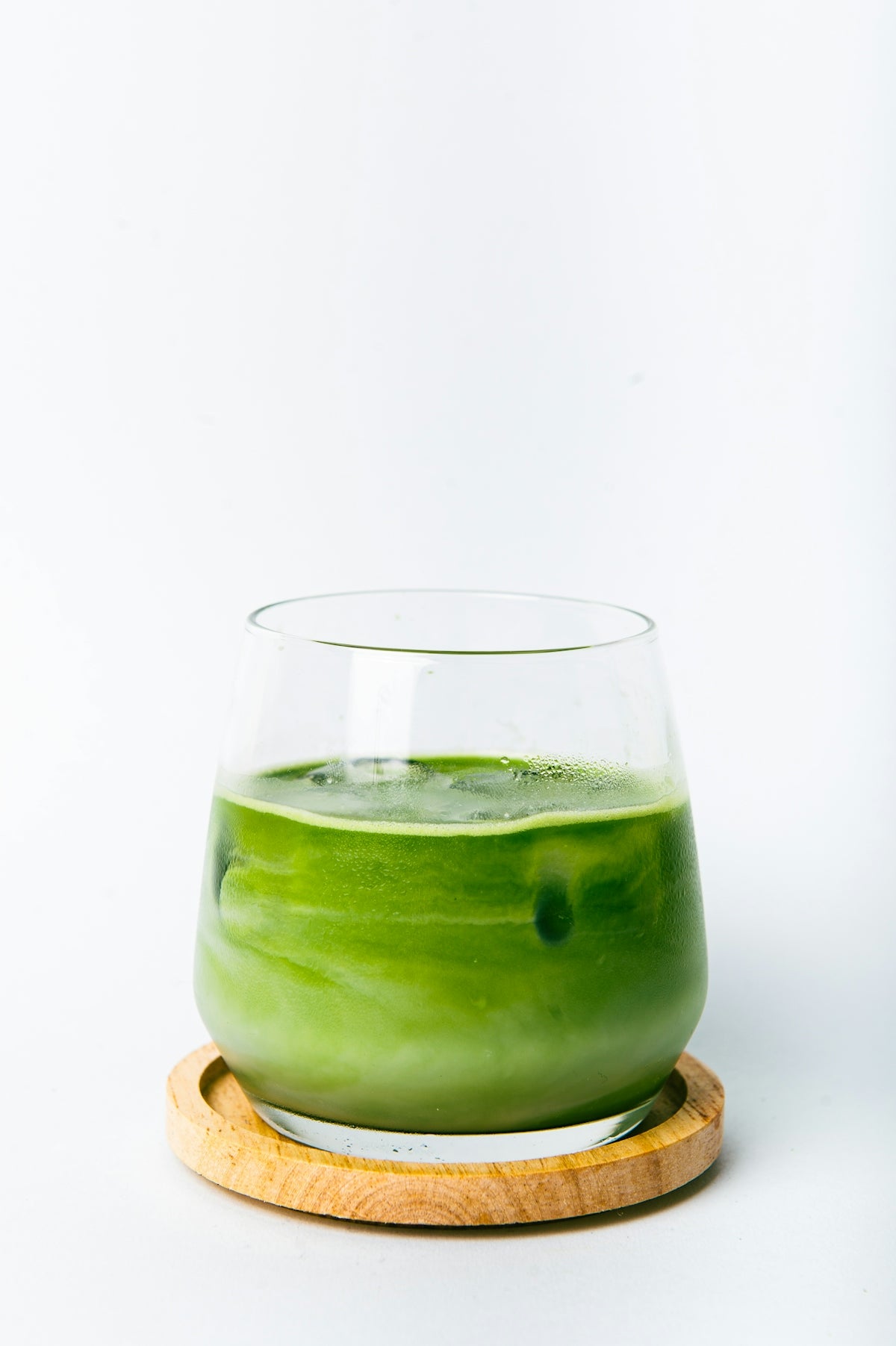 a green liquid in a glass with a wooden coaster