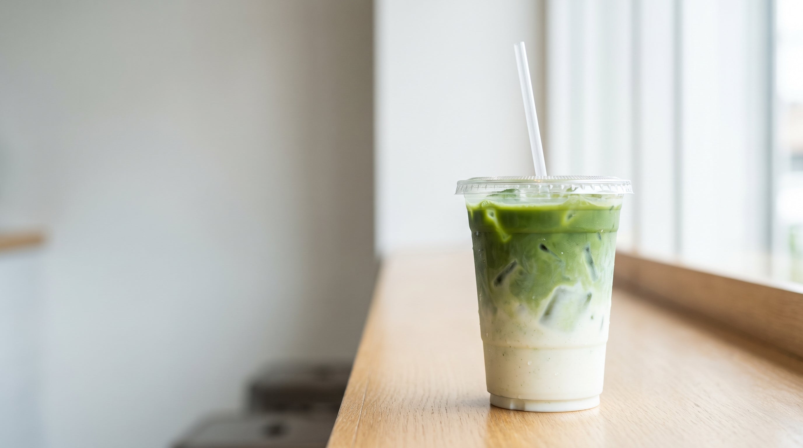 A beautiful iced matcha latte in a clear plastic to go cup on a bright cafe counter