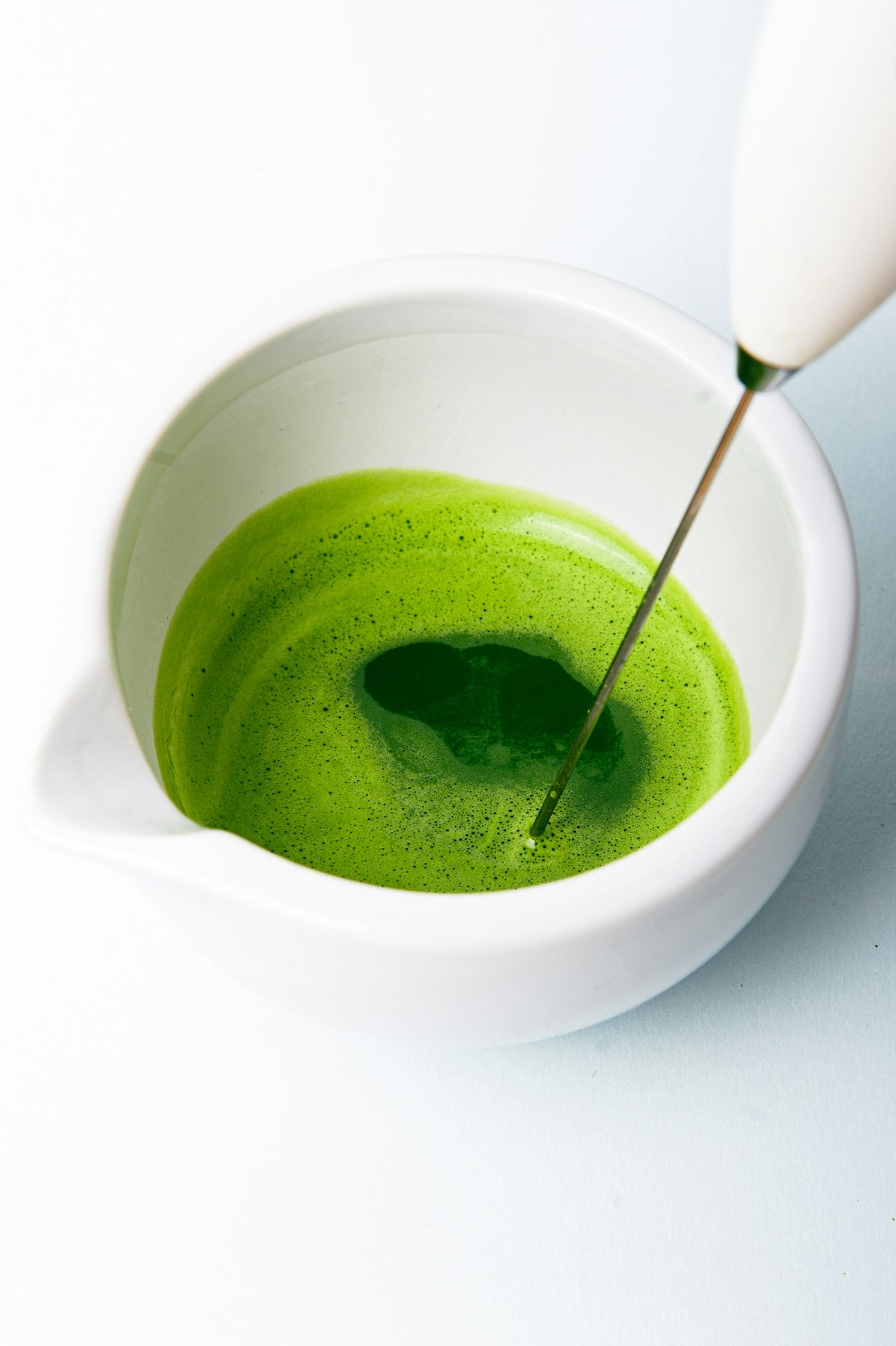 a green liquid in a white bowl with a spoon