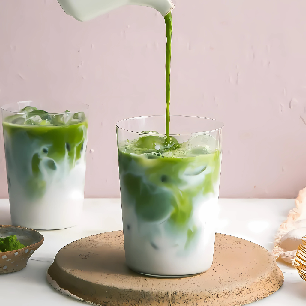 Iced matcha latte poured into a glass over milk and ice on a pink background