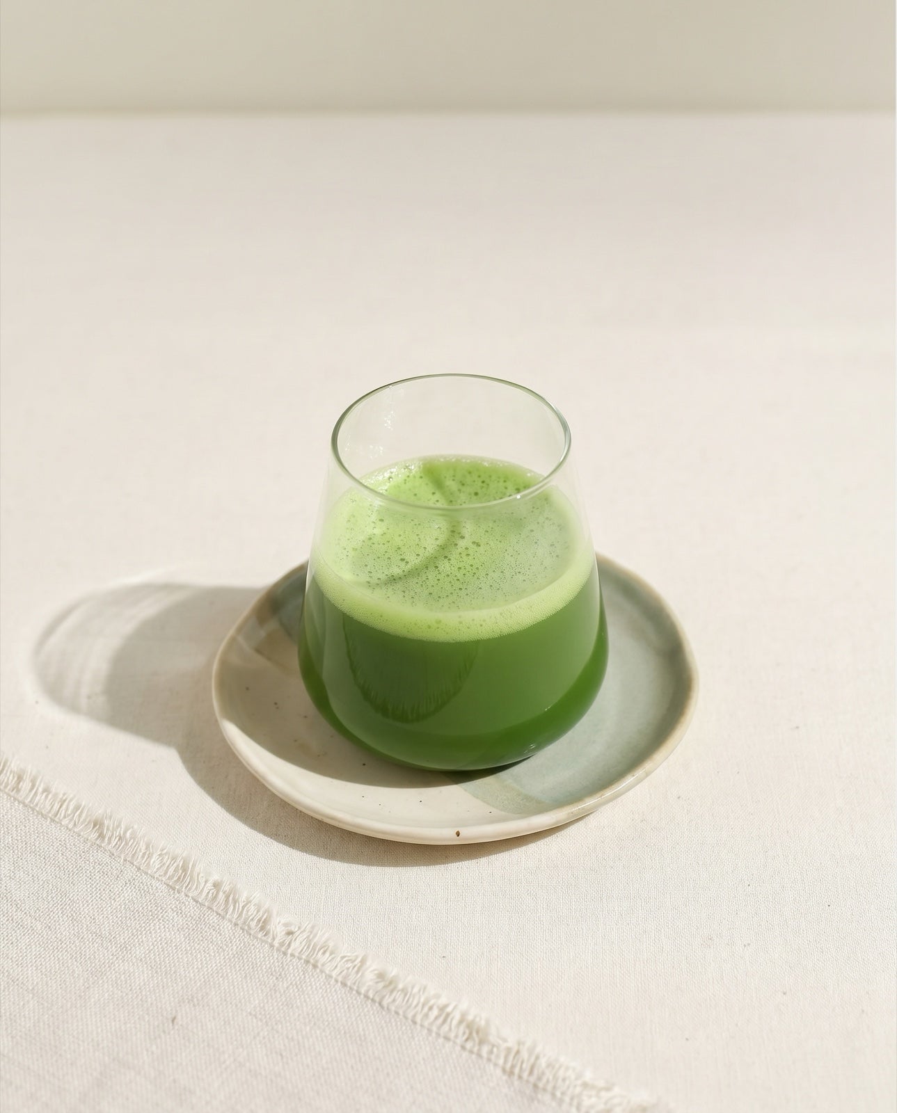 A clean glass of vivid green matcha on a ceramic plate